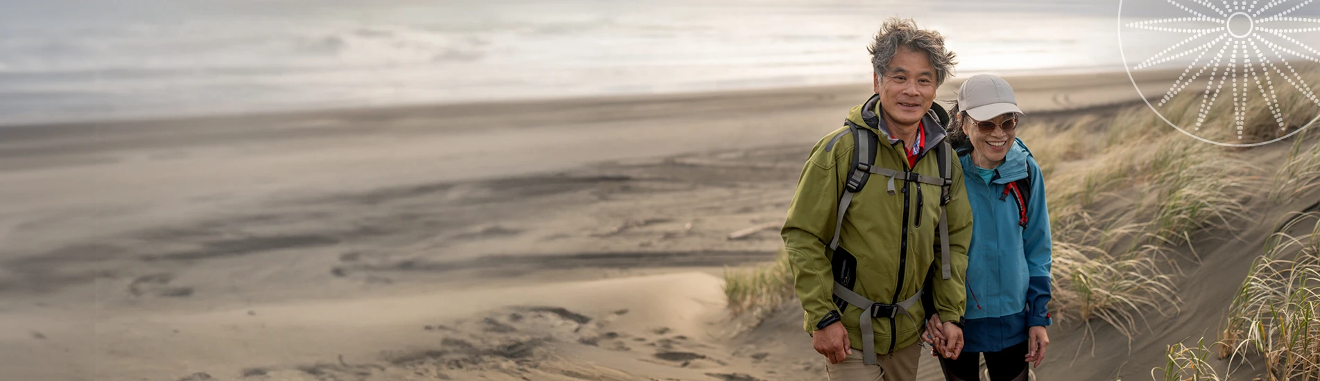 middle-aged couple in rain jackets walking on the beach